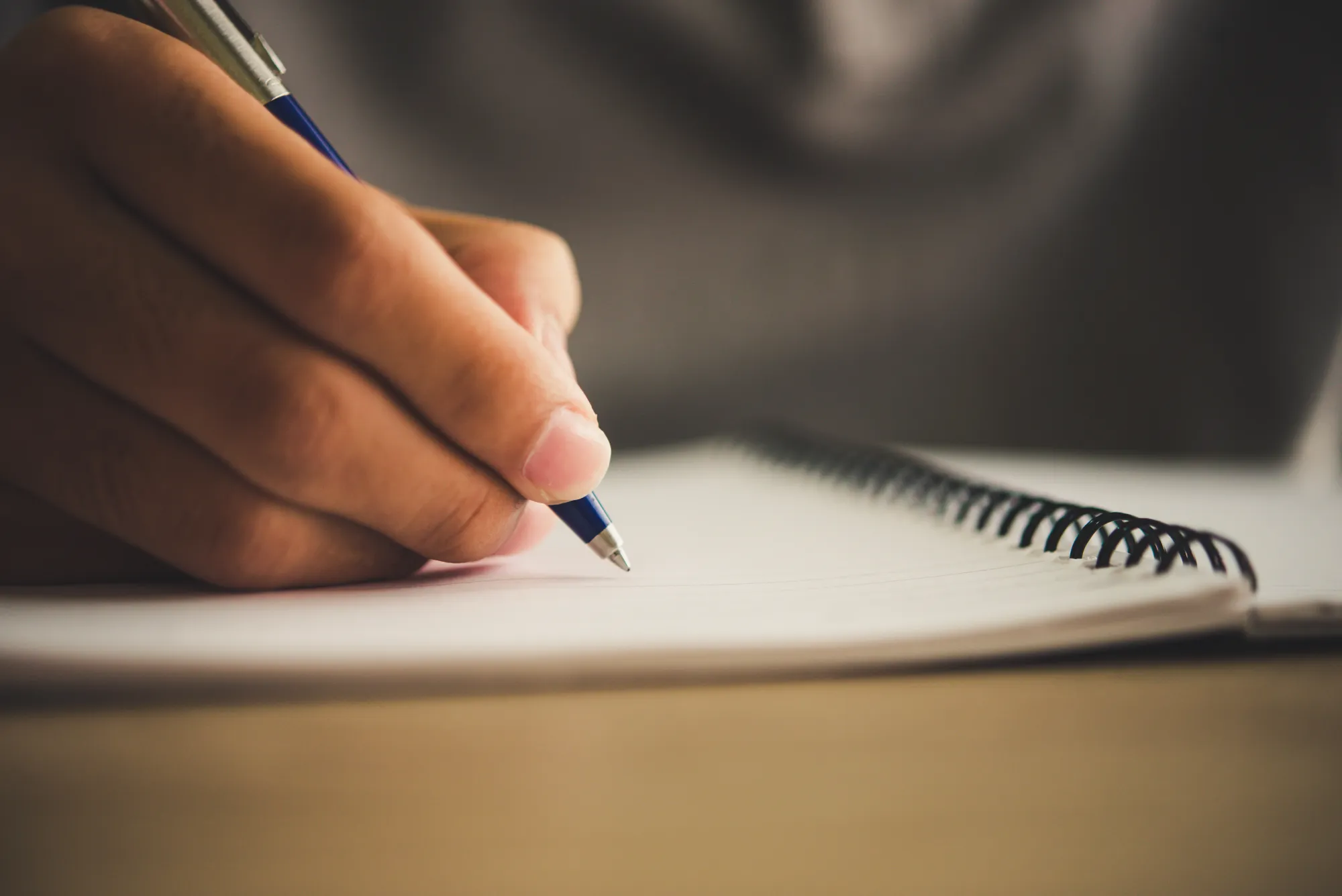 A person's hand with pen writing in a paper journal and not digital journal