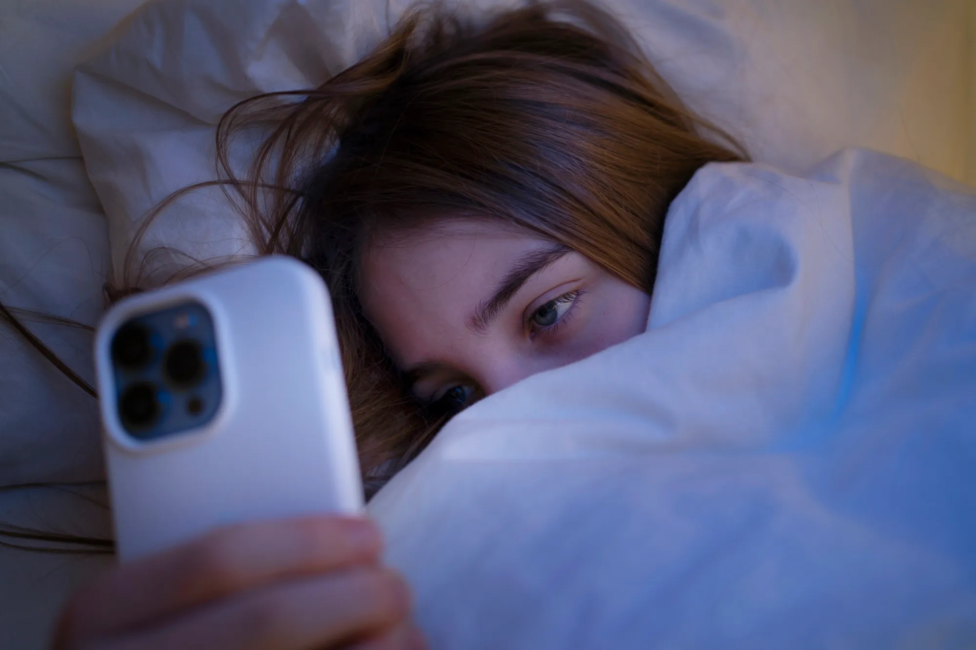 Agirl with tired eyes using phone, remiding herself, "It is time we got to bed."