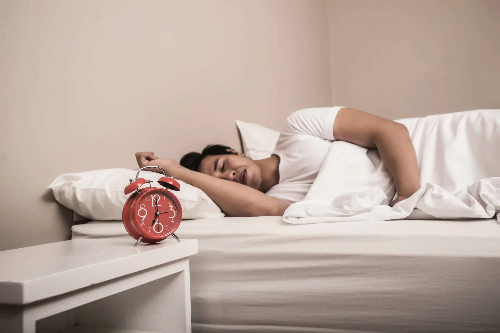 A man with an alarm clock beside him, in his core sleep stage