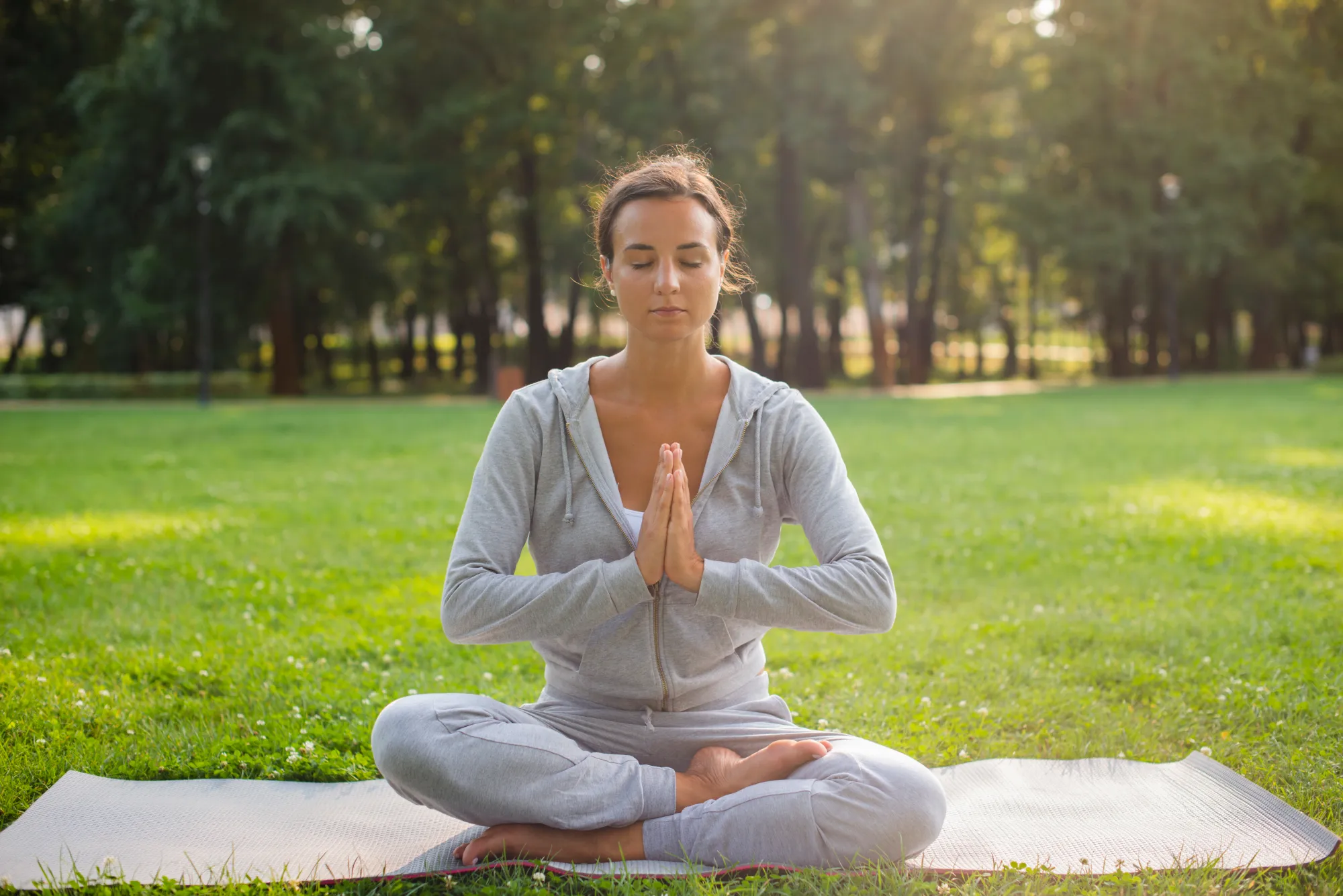 A young woman sitting in a garden on a yoga mat, meditating in nature